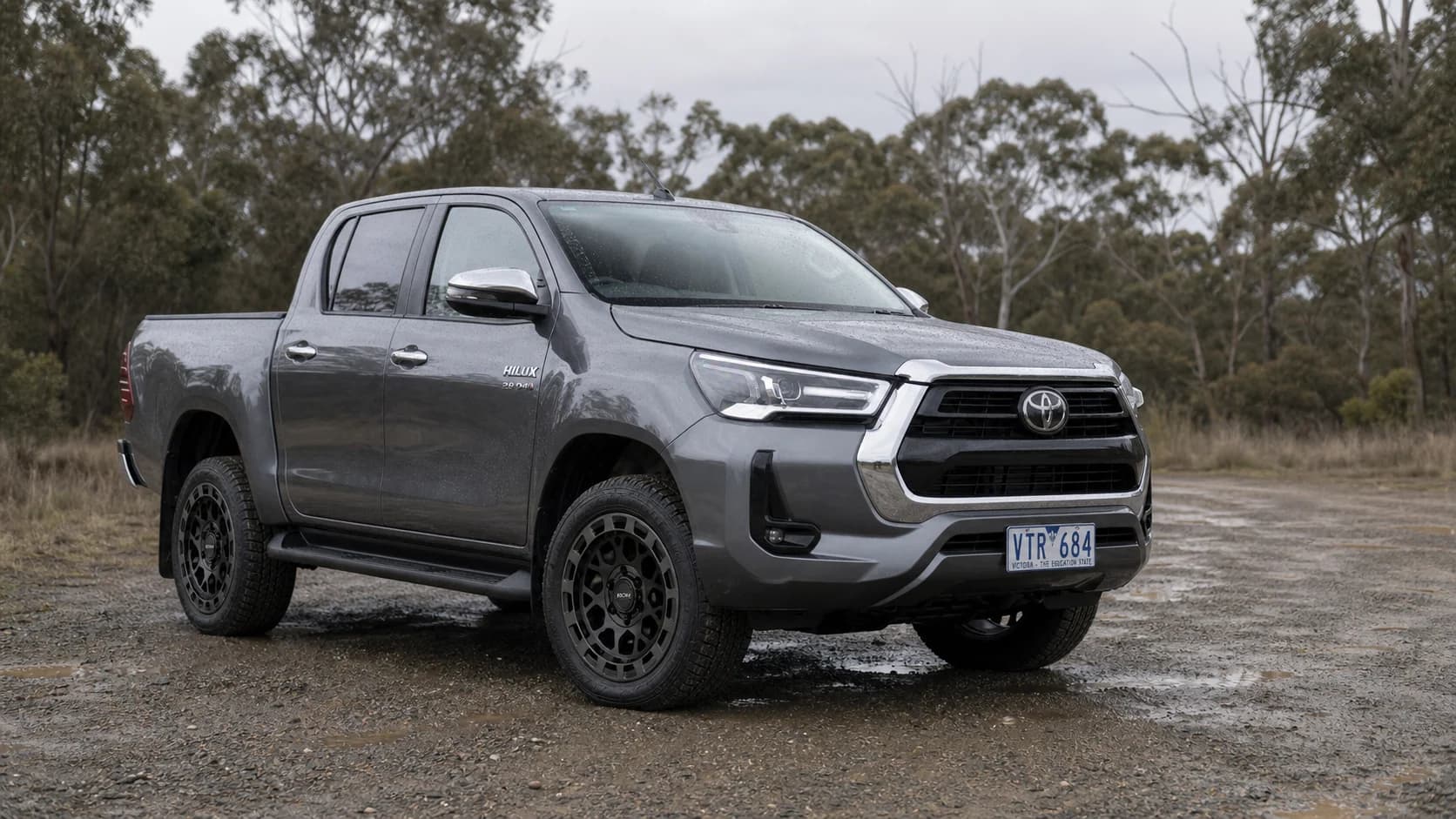 Grey Toyota HiLux N80 fitted with graphite-black ROH Atlas wheels at a wet Victorian gravel pull-off
