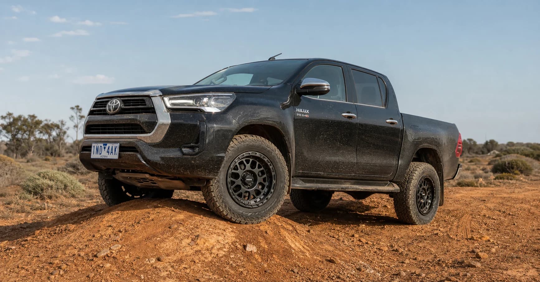 Black standard-track Toyota HiLux N80 on 17-inch graphite wheels and all-terrain tyres articulating over a dry Victorian Mallee trail