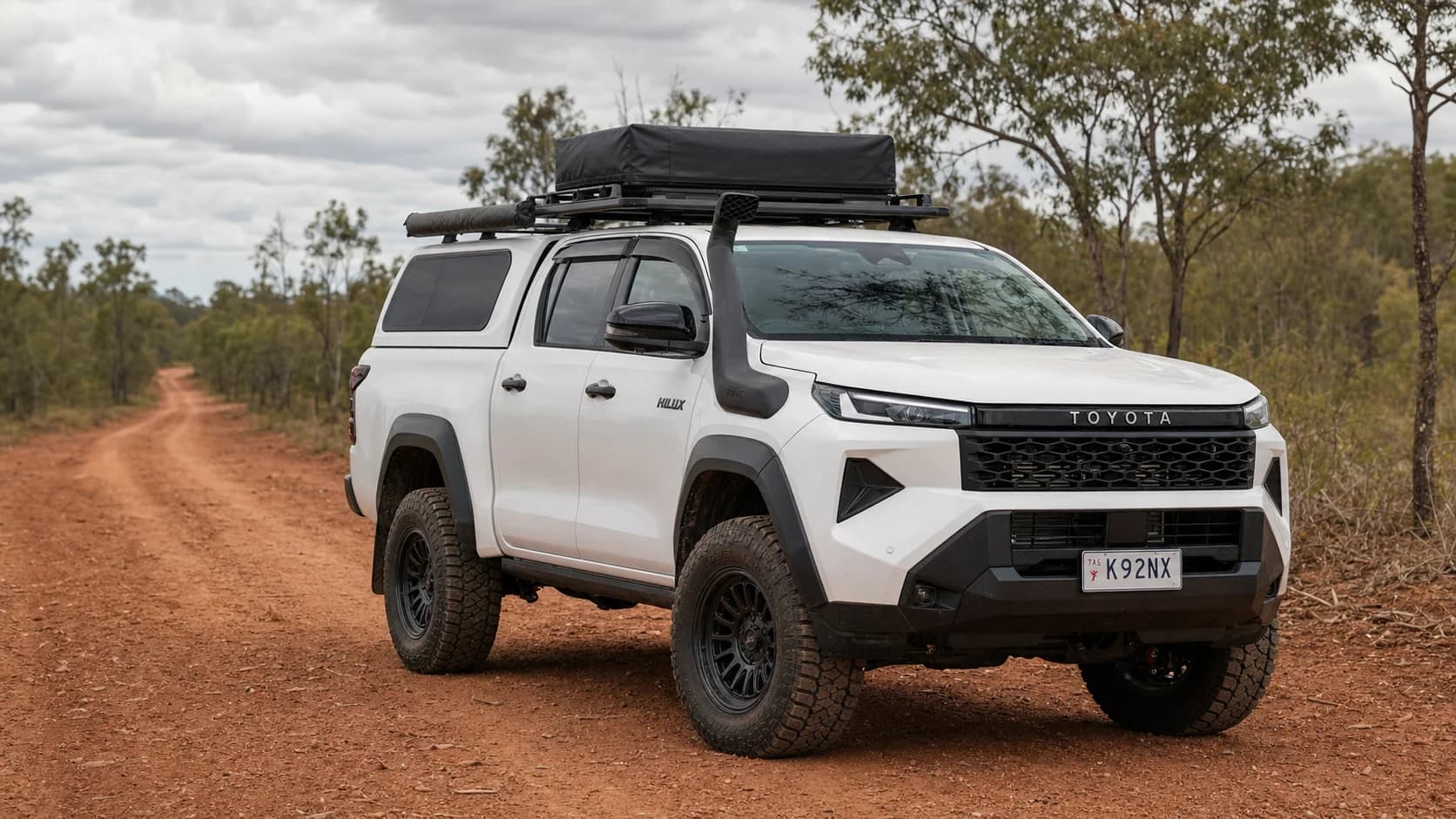 White 2026 Toyota HiLux N90 touring ute with a Tasmanian plate parked on a red Cape York track