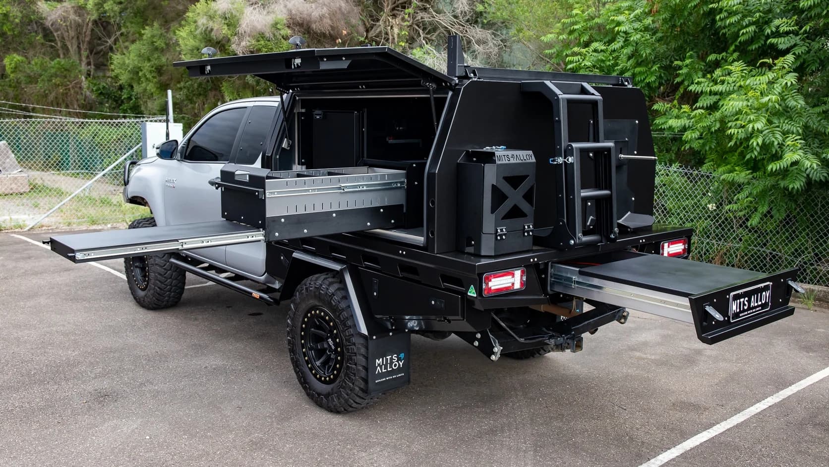 Silver Toyota HiLux extra cab fitted with a black MITS Alloy tray and canopy, gullwing door open to show the internal drawer, jerry can holder and rear slide-out trays