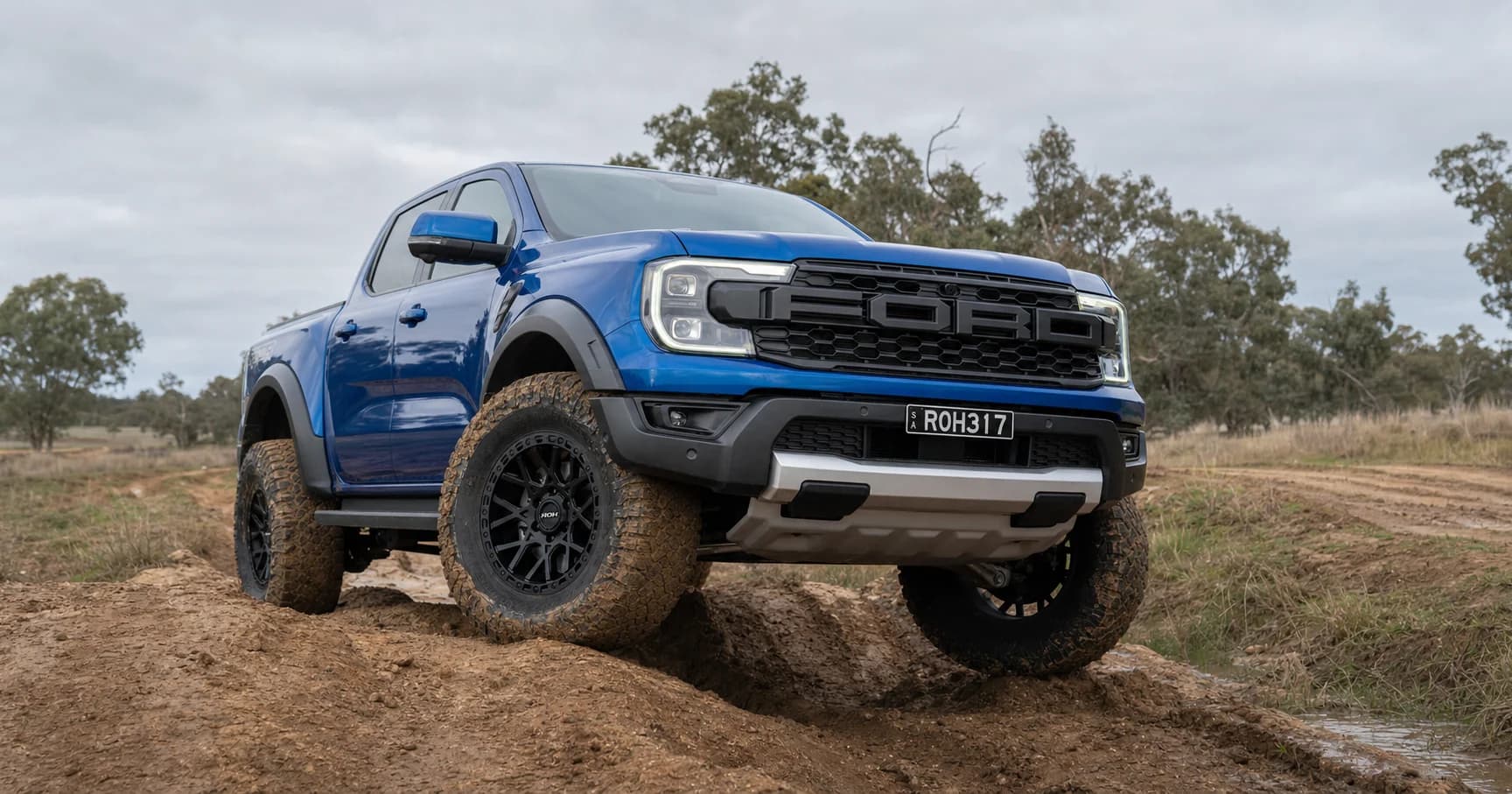 Blue Ford Ranger Raptor fitted with matte-black ROH Crawler wheels articulating across muddy South Australian ruts