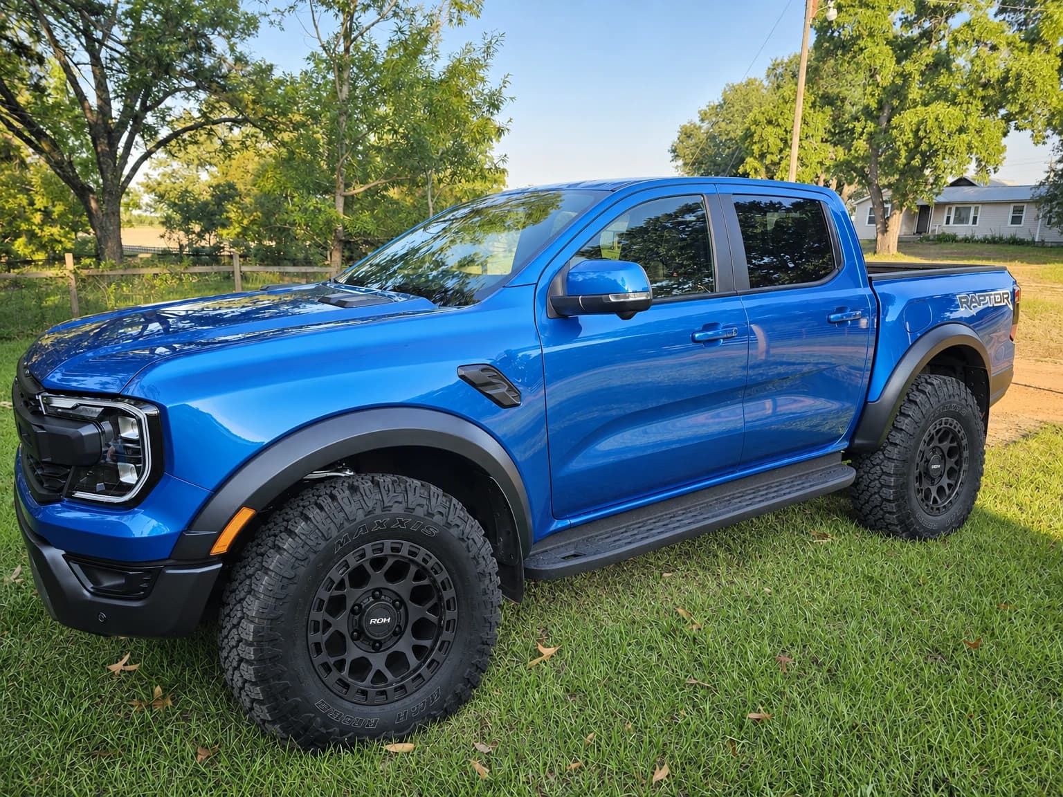 Blue Next-Gen Ford Ranger Raptor with dark ROH wheels and off-road tyres parked on grass