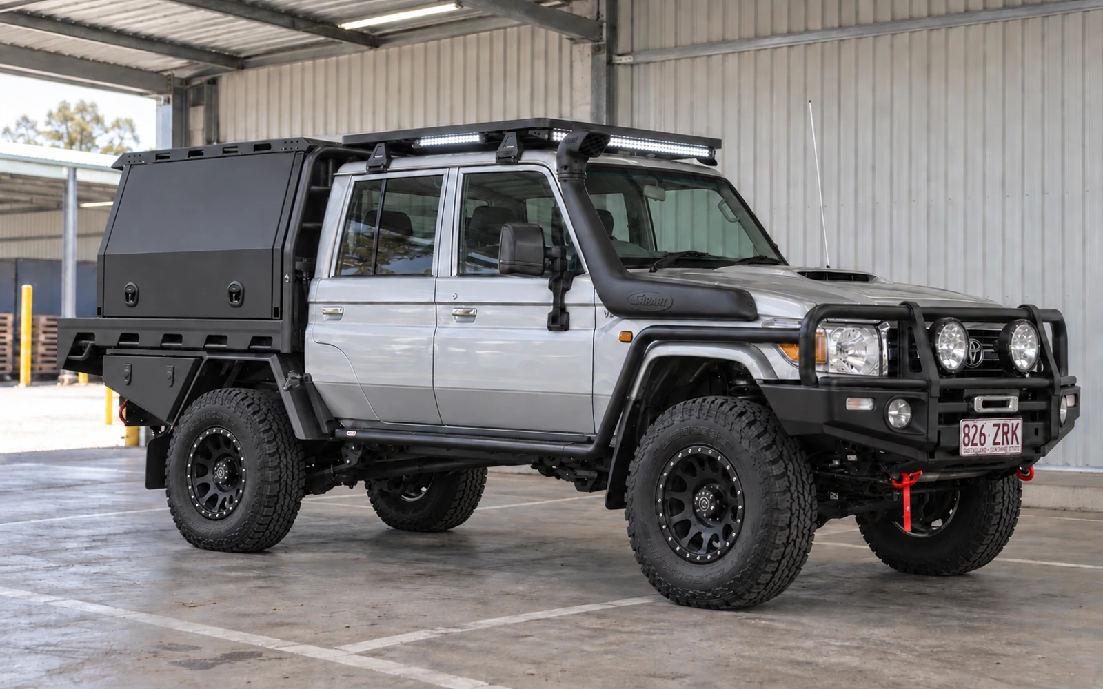 Silver Toyota LandCruiser 79 Series dual cab with a black MITS Alloy canopy, black wheels, off-road tyres, bull bar, Safari snorkel and illuminated roof lights